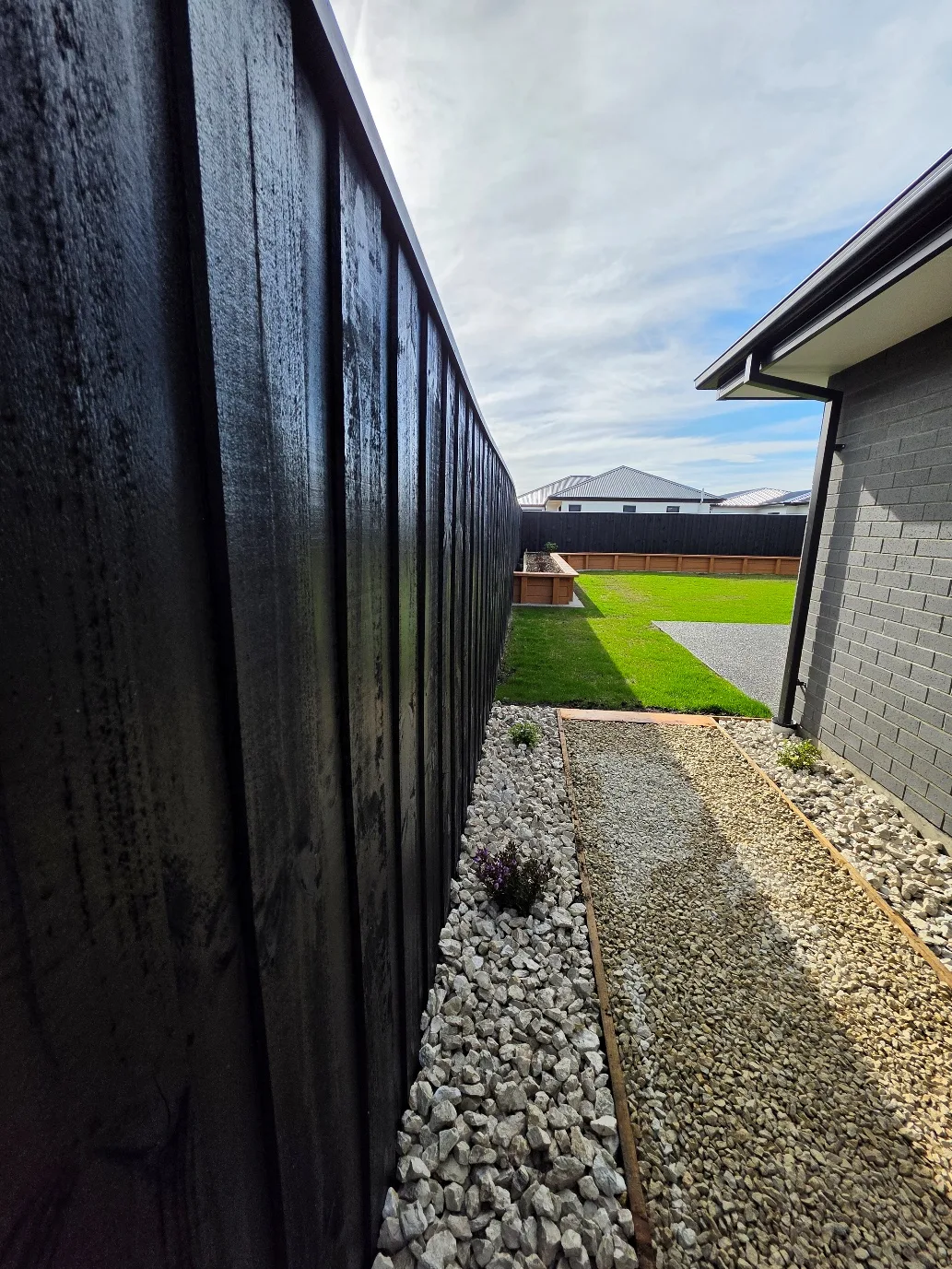 Side yard landscaping with black timber fencing, decorative gravel borders, fresh lawn and raised planter beds by Kings Works in Christchurch